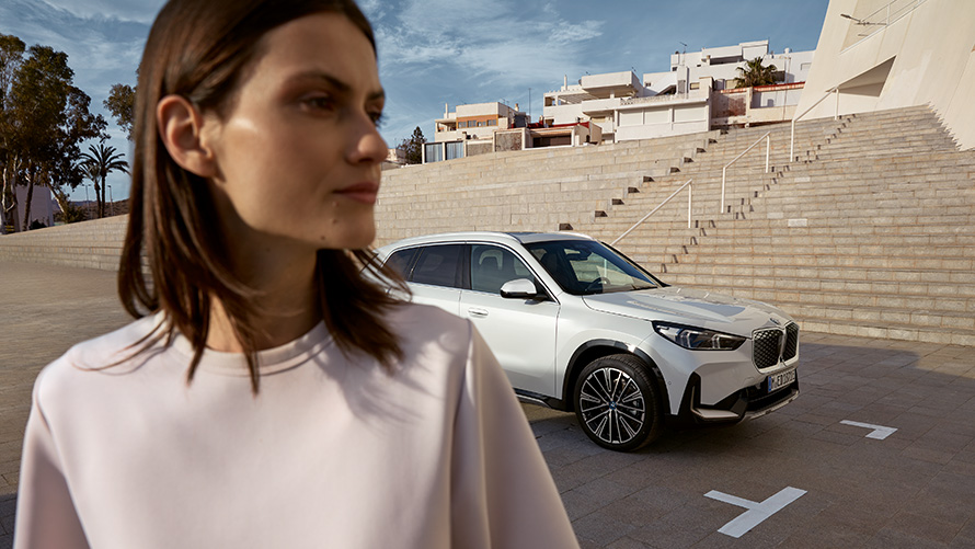 BMW iX1 xDrive30 U11 BEV 2022 BMW Financial Services BMW Financial Services woman and BMW iX1 xDrive30 U11 BEV in front of stairs